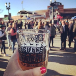 a hand holding a "Beerfest in the Ballpark" glass with the lugnuts stadium in the background